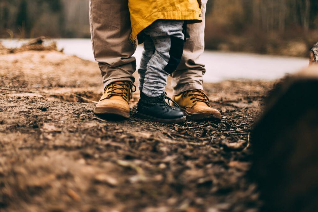 Close up shot of adult and child's boots in a dirt-covered area