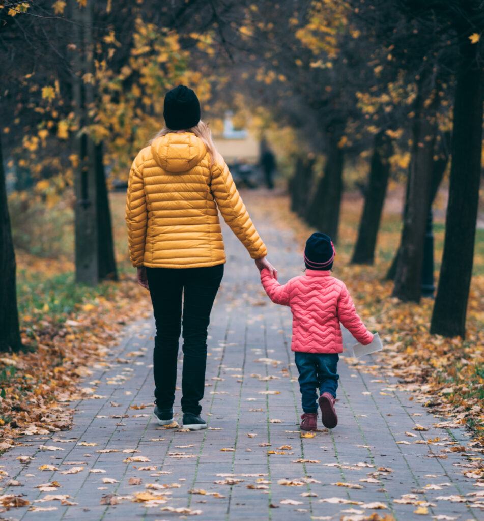A mother and her child strolling along a scenic autumn path, surrounded by colorful leaves and the beauty of nature.
