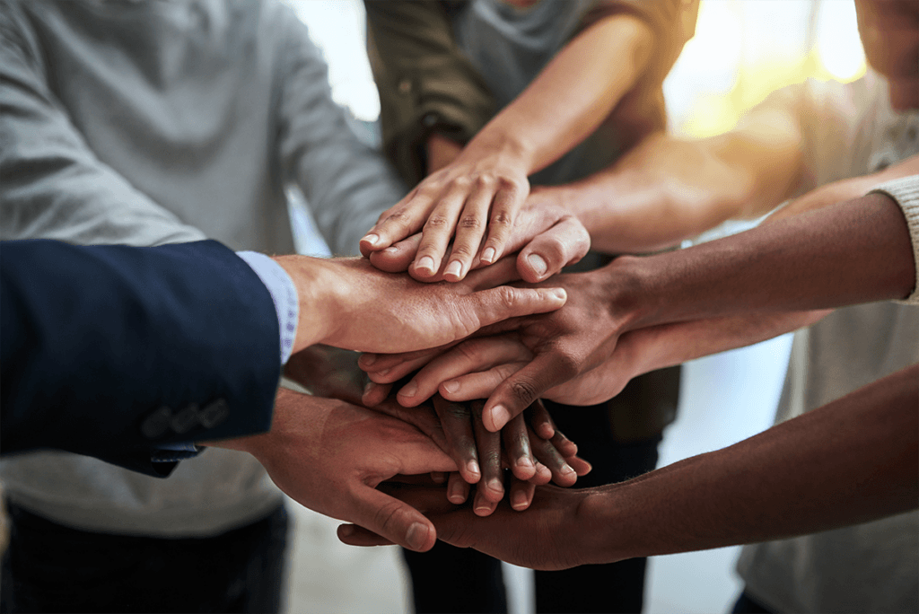 A diverse group of people standing in a circle, joining their hands together in unity and solidarity.