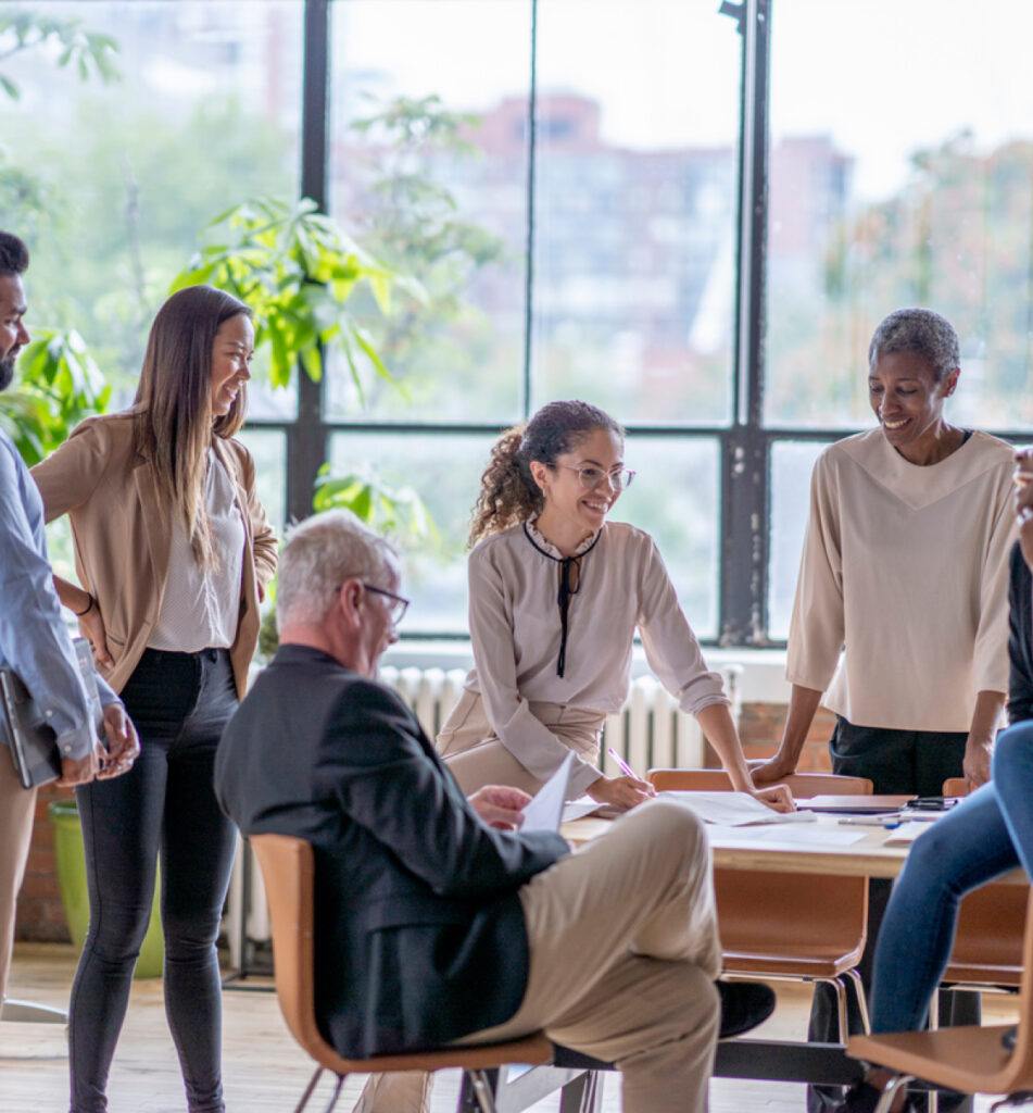 A group of people standing and smiling in an office meeting, discussing ideas and collaborating.