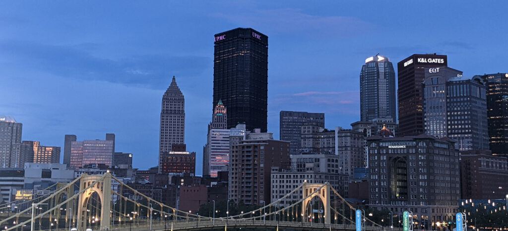 City of Pittsburgh skyline at night with a yellow bridge in front, showcasing the vibrant city lights.