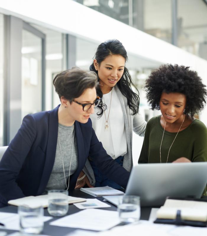 Three women discussing while looking at a laptop