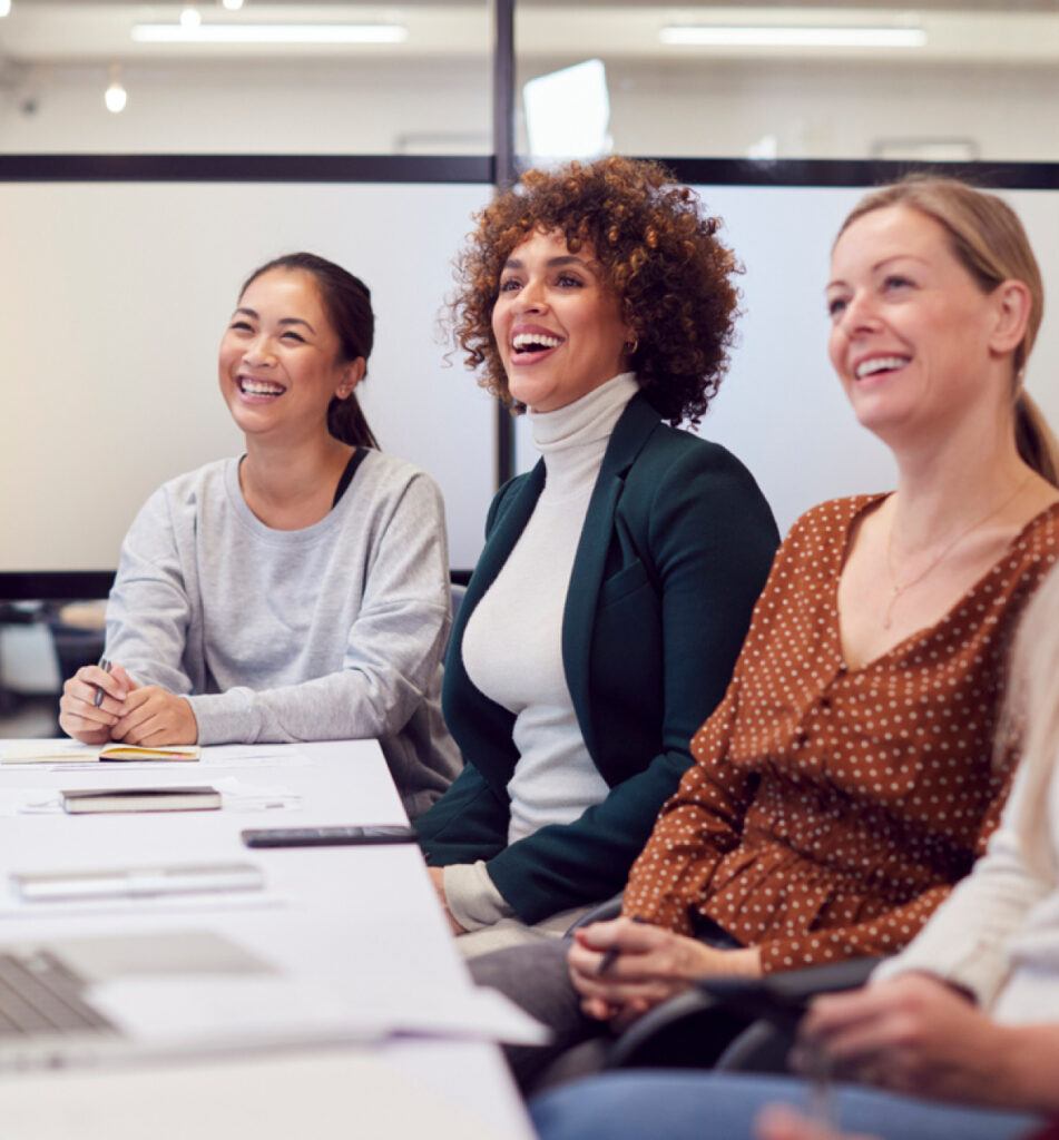 Five women sitting at a table in an office, engaged in a professional discussion and working collaboratively.