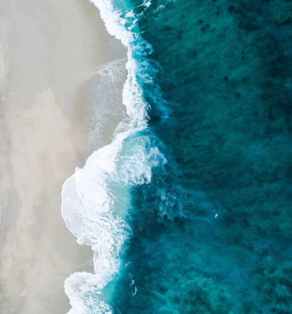 An amazing view from above, capturing the vastness of the ocean and the golden sand below.